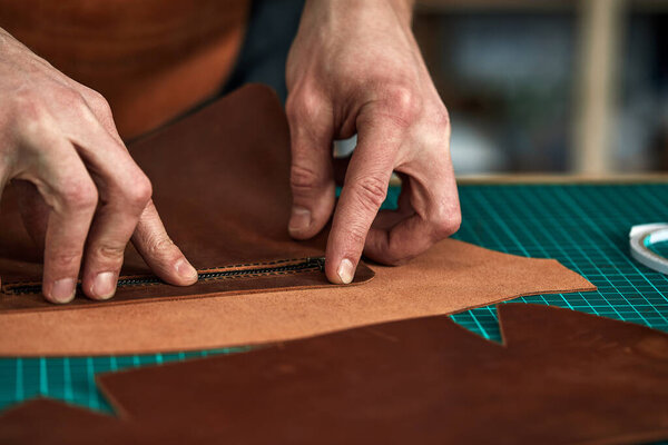 Tailors hands a purchase plan, a partner tries on a detail of a leather product, a leather steam room collects a leather bag from parts, a tailor business