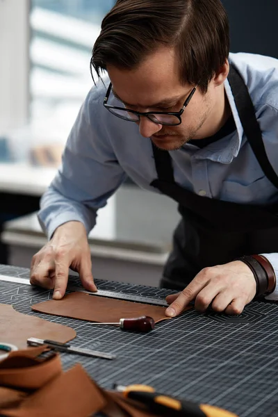 leather craftsmen working making measupenets in patterns at table in workshop studio