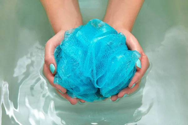 Mains féminines tenant un chiffon de toilette synthétique doux rond dans le bain avec de l'eau. Les mains en gros plan. Soins spa, soins du corps, fond d'eau — Photo