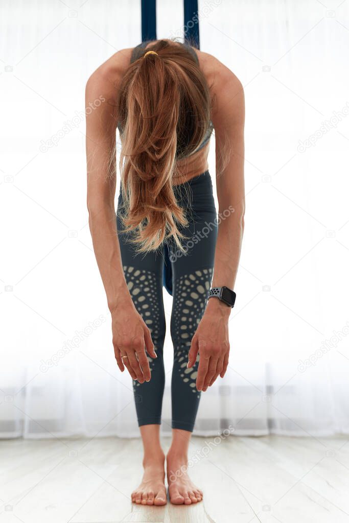 Fit pretty young woman doing fly yoga stretching exercises in fitness training white gym loft classroom.