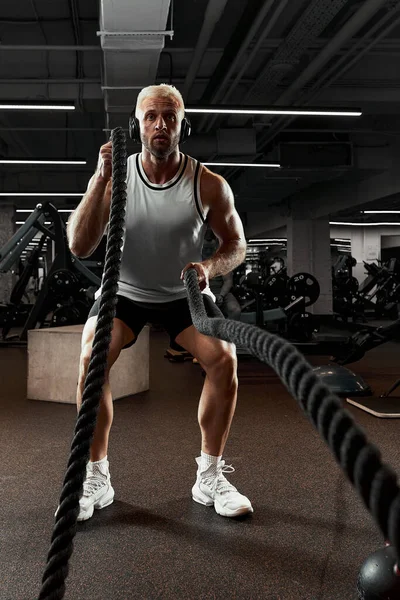 Sport. Strong man exercising with battle ropes at the gym with. Athlete doing battle rope workout at gym. Dramatic sports background. — Stock Photo, Image