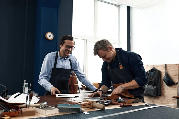 Two young leather craftsmen, joy and joke while working in the workshop, positive leather tailors, have fun at work. Family small business. — Stock Photo, Image