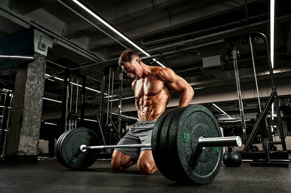 Atelt avec un corps magnifiquement sculpté se prépare à faire des exercices avec un haltère. L'athlète prépare l'haltère pour travailler les muscles. Blessures sportives, échauffement avant entraînement — Photo