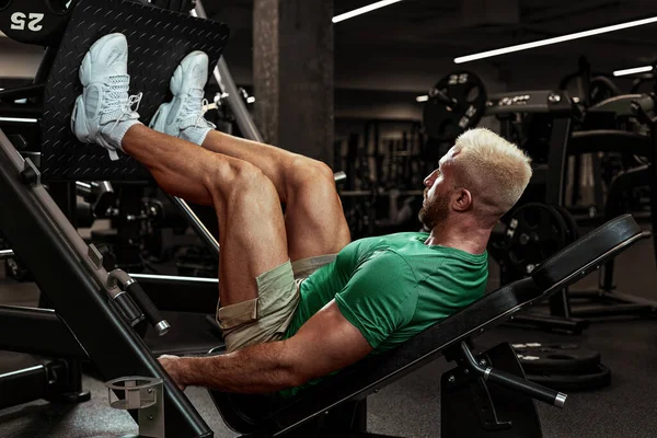Atleta joven inflado haciendo ejercicios de piernas en el gimnasio, piernas oscilantes, equilibrio de masa muscular, calentamiento antes del entrenamiento —  Fotos de Stock