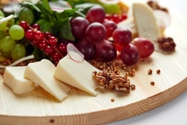 Assortment of cheeses and grapes on a wooden background, close-up, light background, mix of Italian cheeses in backlight. — Stock Photo, Image