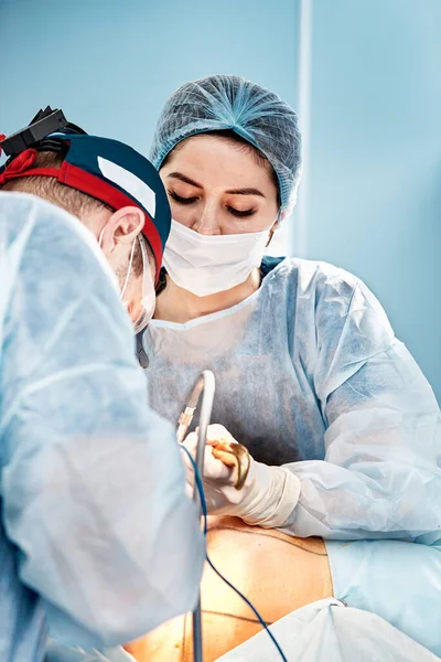 Cirujanos operan a un paciente anestesiado suturando una herida rodeada por una segunda mujer cirujana —  Fotos de Stock