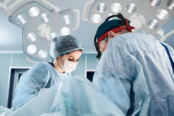 현대 수술실에서 밝은 빛을 받으며 수술 즉 현대 의학을 하는 일단의 남녀 외과의들이 있다. — 스톡 사진