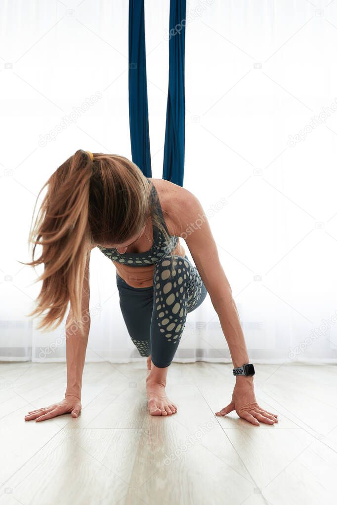 Woman doing anti-gravity aero yoga in a room with air hammocks, doing warm-up and stretching before training in air hammocks