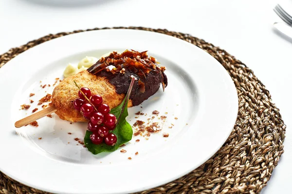 Juicy Kiev cutlet with mashed potatoes, close-up of Kiev cutlet decorated with a leaf of lettuce and berries on a light background in a light dish