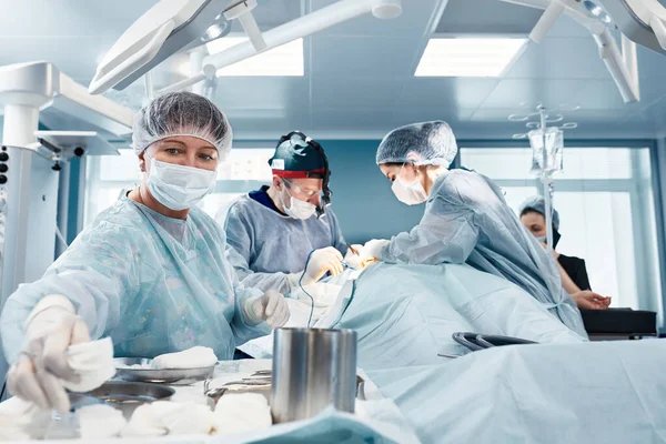 Uma operação real, uma mulher cirurgiã dá instrumentos, durante uma operação plástica, contra o pano de fundo de uma equipe de cirurgiões em uma unidade cirúrgica moderna, salvando vidas. — Fotografia de Stock