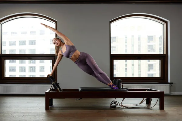 A woman yoga instructor trains on a reformed Cadillac in a large hall against a window, modern equipment for training in gyms, correction of the musculoskeletal system. — Stock Photo, Image