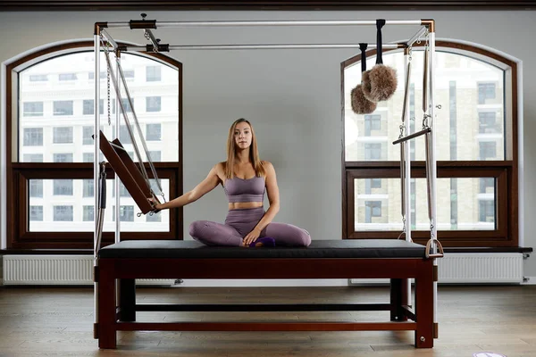 Girl instructor on reformer cadillac, posing, showing exercises for spine correction, modern reformer equipment for fitness centers. — Stock Photo, Image