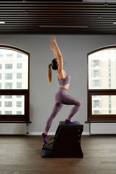 Una mujer instructora de yoga entrena en un barril de reformador contra la ventana, corrección del sistema musculoesquelético en equipos modernos de reformador, corrección del sistema musculoesquelético. — Foto de Stock