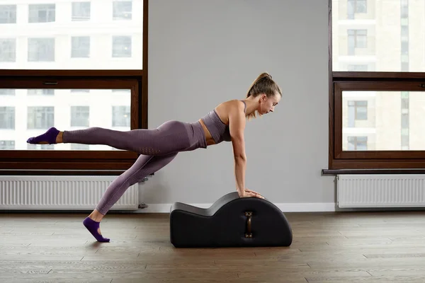 A woman yoga instructor trains on a reformed cadilac in a large hall against a window, modern equipment for training in gyms, correction of the musculoskeletal system. — Stock Photo, Image