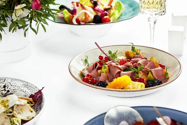 Duck breast salad, Cold smoked duck breast in salad with oranges and apples and red berries, on a wedding table, with white tablecloths.
