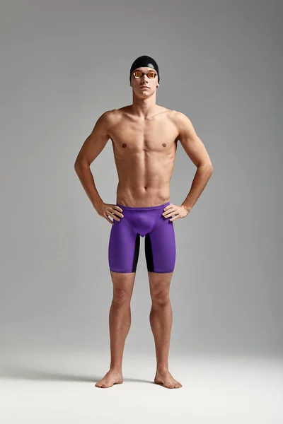 A male swimmer stands with crossed arms, on a gray background, challenging, spears space
