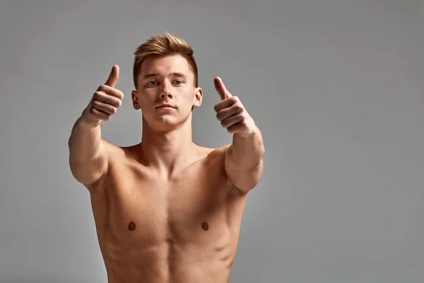 Ein Schwimmer, ein junger Athlet in hervorragender körperlicher Verfassung, zeigt mit seiner Hand, die zum Training drängt, ein Werbebanner, einen grauen Hintergrund, eine Kopie des Raumes. — Stockfoto