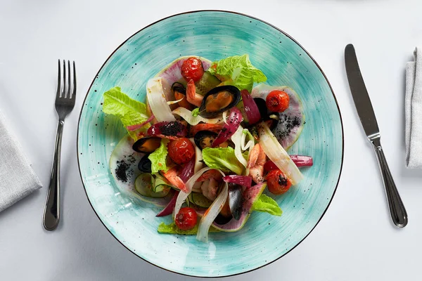 Vongole aux moules avec salade, moules cuites dans une sauce au vin blanc, entrée aux moules avec couverts sur fond clair, vue sur le dessus. — Photo