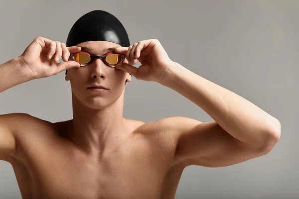 Joven nadador masculino preparándose para el inicio, retrato de cerca de un nadador en una máscara y un sombrero, fondo gris, espacio para copiar, concepto de natación. — Foto de Stock