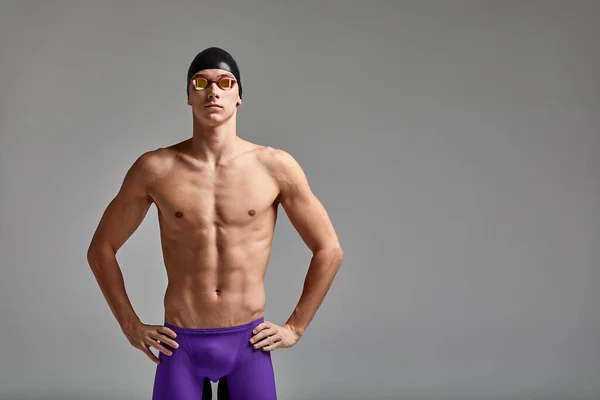 Jovem nadador do sexo masculino se preparando para o início, metade do comprimento retrato de um nadador em uma máscara e um chapéu, fundo cinza, espaço de cópia, conceito de natação. — Fotografia de Stock