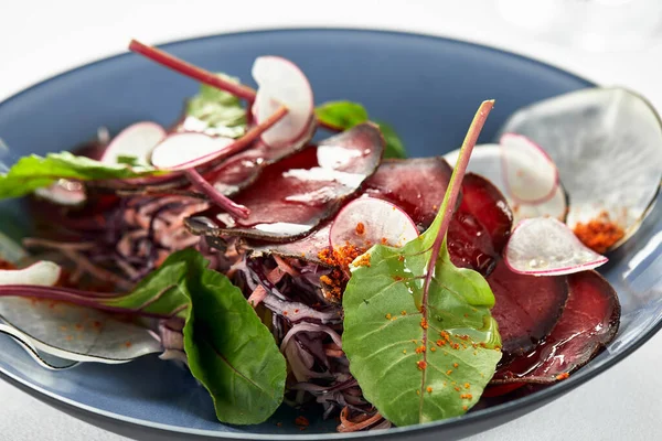 Bresaola, in dünne Scheiben geschnitten mit Salat und püriertem gesalzenem Rindfleisch in einem Teller mit Sauce und Rote-Bete-Blättern aus nächster Nähe — Stockfoto