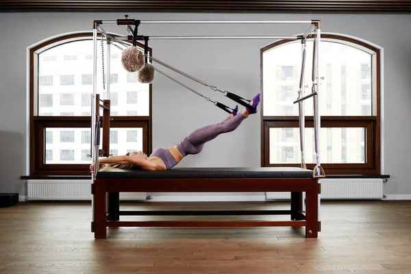 Pilates aerobics instructor woman in fitness exercise on cadillac reformer, musculoskeletal system training on modern reformer simulator. — Stock Photo, Image