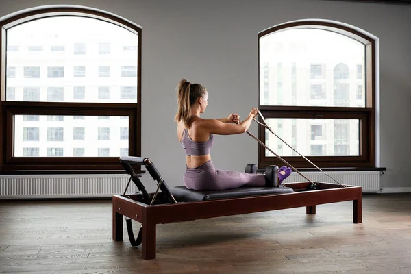 Genç bir kız ıslah yatağıyla pilates egzersizi yapıyor. Gri arka planda güzel ince fitness antrenörü, gösterişsiz anahtar, sanat ışığı, fotokopi alanı reklam afişi — Stok fotoğraf