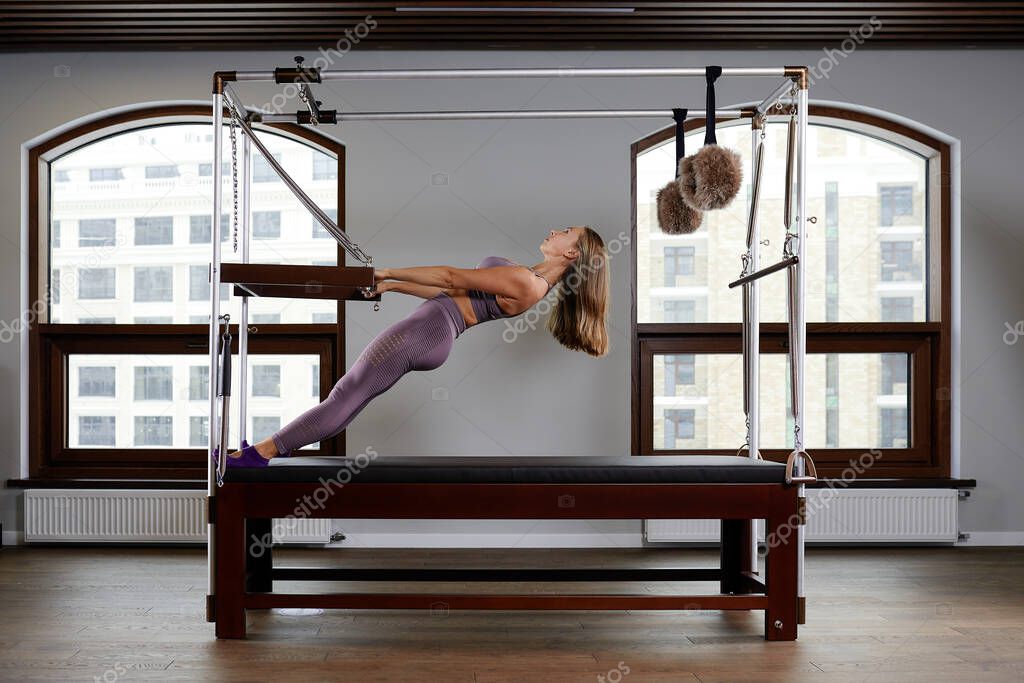 Pilates instructor on the cadilak reformer, a woman trainer in excellent shape works on a modern reformer, the study of the musculoskeletal apparatus on modern reformer simulators