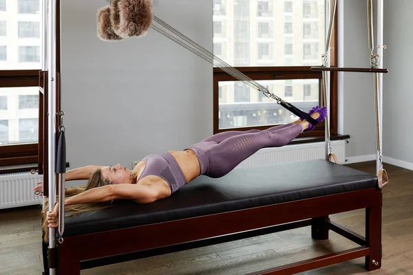 Uma jovem faz exercícios de pilates com um reformador de cama