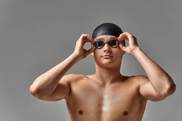 Ung manlig simmare förbereder sig för start, närbild porträtt av en simmare i en mask och en hatt, grå bakgrund, kopiera utrymme, simning koncept. — Stockfoto