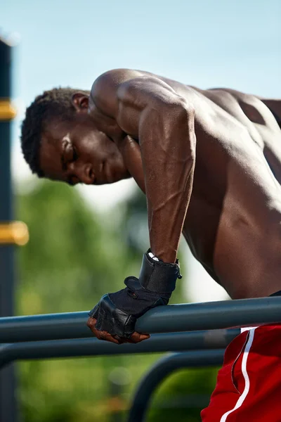 Schwarzer Fitnessmann, der auf dem unebenen Barren trainiert, Rückenstrecktraining eines männlichen Modells in urbaner Umgebung. Ein Afrikaner in seinen Zwanzigern trainiert auf der Straße. — Stockfoto