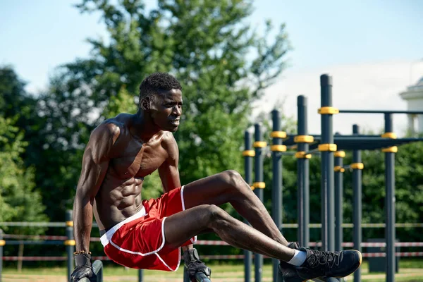 Hombre de fitness negro haciendo ejercicio inmersiones, entrenamiento cruzado de modelo masculino en ambiente urbano. Un africano de unos veinte años está entrenando en la calle.. — Foto de Stock