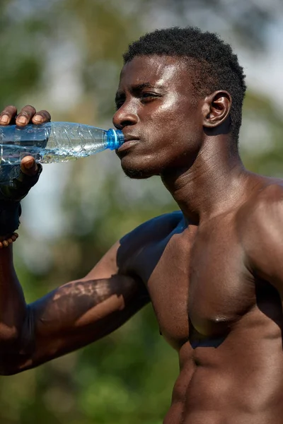 Hombre afroamericano joven bebe agua mientras entrena en el parque en el campo de deportes, concepto de entrenamiento al aire libre, crossfit — Foto de Stock