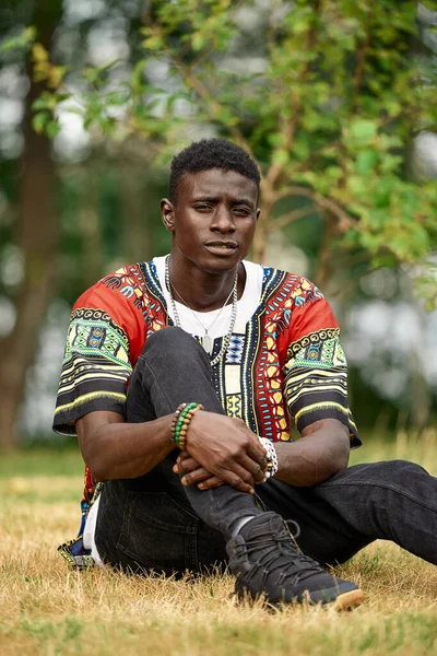 Un homme noir se repose dans le parc, un homme noir attrayant est assis sur l'herbe dans l'air frais, la détente est le repos, l'unité avec la nature. — Photo