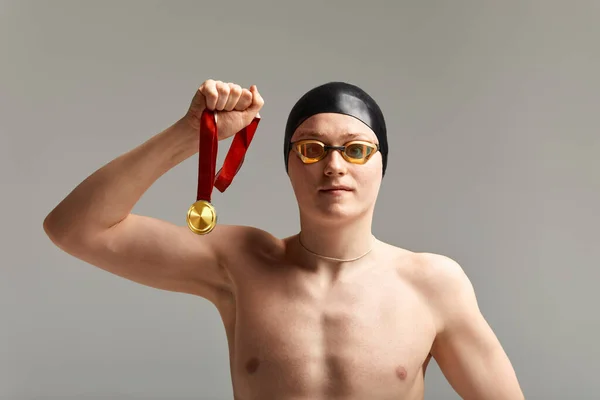 Pływak z medalem na szarym tle raduje się zwycięstwem, sportowiec w doskonałej kondycji fizycznej świętuje zwycięstwo trzymając medal w ręku, koncepcja zwycięstwa, szare tło, przestrzeń do kopiowania — Zdjęcie stockowe