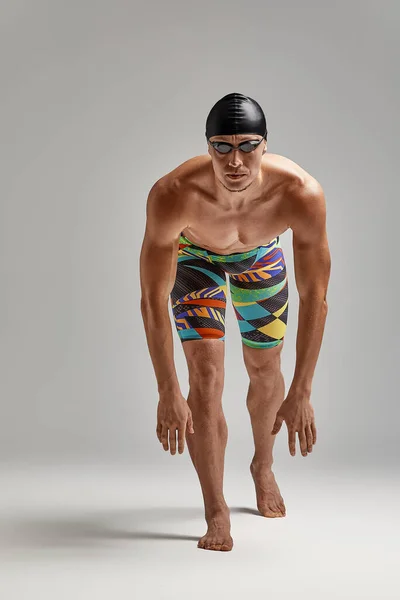 Um nadador em calções de banho se prepara para o início, um atleta em um fundo cinza se prepara para um mergulho, eu faço uma pose para um mergulho na piscina, usando óculos e uma máscara. — Fotografia de Stock