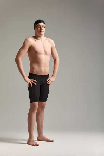 Jovem nadador atraente em excelente forma física em shorts de natação roxo, em um fundo cinza, espaço de cópia — Fotografia de Stock