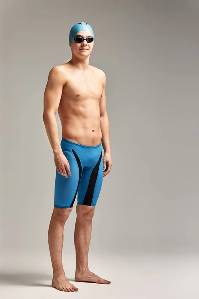 Portrait of a swimmer in a cap and mask, full-length portrait, young athlete swimmer wearing a cap and mask for swimming, copies of space, gray background