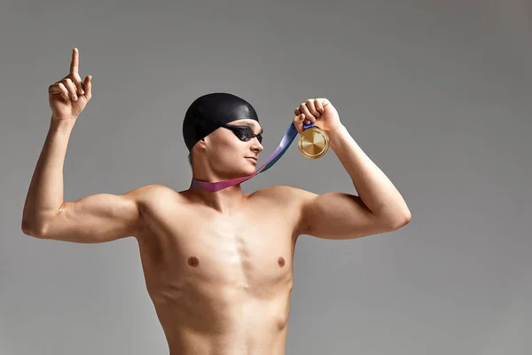 Pływak z medalem na szarym tle raduje się zwycięstwem, sportowiec w doskonałej kondycji fizycznej świętuje zwycięstwo trzymając medal w ręku, koncepcja zwycięstwa, szare tło, przestrzeń do kopiowania — Zdjęcie stockowe