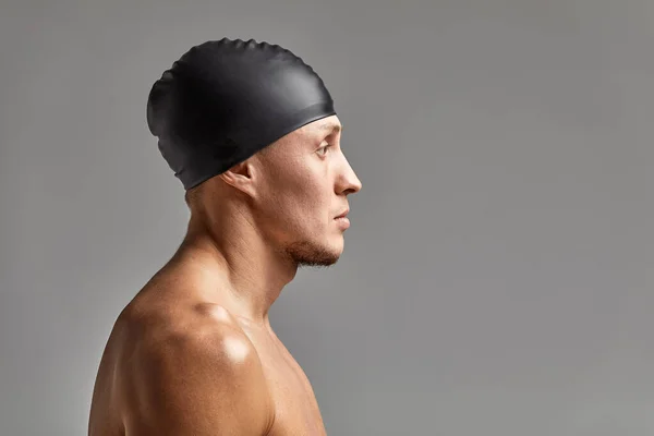 Portret młodego pływaka w gumowej czapce, stojącego na szarym tle kapelusza przygotowującego się do treningu — Zdjęcie stockowe