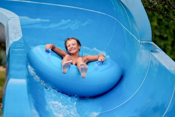 Feliz um menino de 8 anos está montando no parque aquático em círculos infláveis em escorregas de água com respingo — Fotografia de Stock