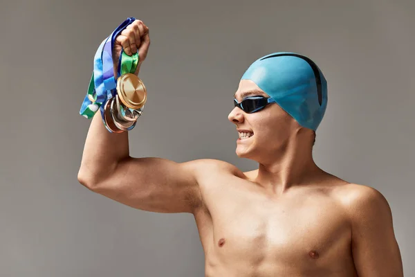 Nadador com uma medalha em um fundo cinza se alegra na vitória, um atleta em excelente forma física celebra uma vitória segurando uma medalha em sua mão, conceito de vitória, fundo cinza, espaço de cópia — Fotografia de Stock