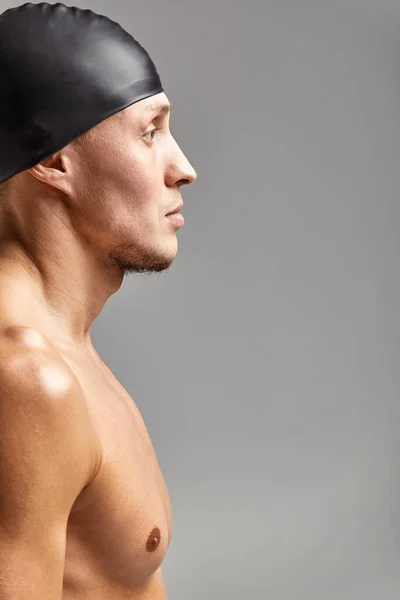 ゴム製の帽子をかぶった若い男の水泳の肖像画、トレーニングの準備ができて灰色の背景の帽子に立って、プロフィールビュー — ストック写真