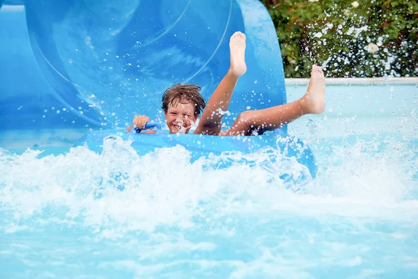 Feliz um menino de 8 anos está montando no parque aquático em círculos infláveis em escorregas de água com respingo — Fotografia de Stock