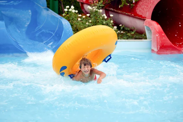 8 살짜리 남자 아이가 워터 파크에서 물을 튀기는 슬라이드에 부풀어 오르는 원을 타고 있는 것 이 행복하다. — 스톡 사진