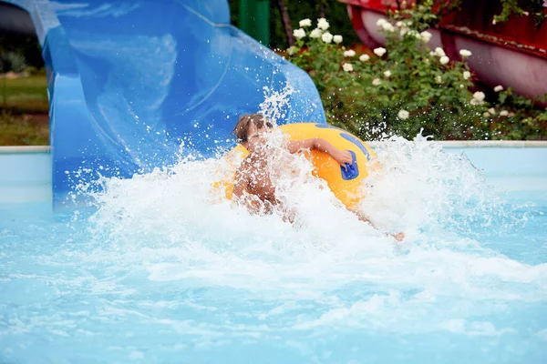 Feliz um menino de 8 anos está montando no parque aquático em círculos infláveis em escorregas de água com respingo — Fotografia de Stock