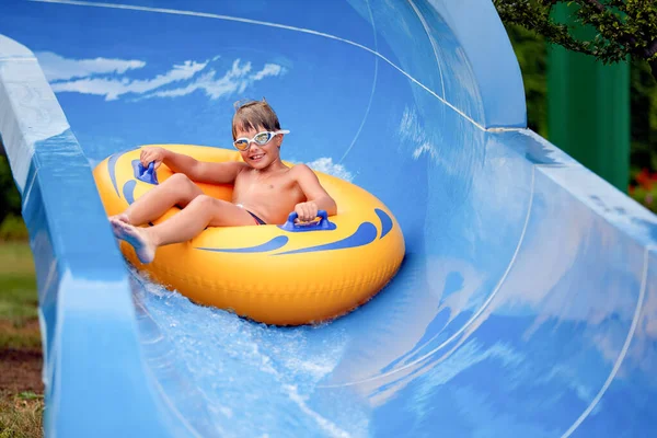 Feliz um menino de 8 anos está montando no parque aquático em círculos infláveis em escorregas de água com respingo — Fotografia de Stock