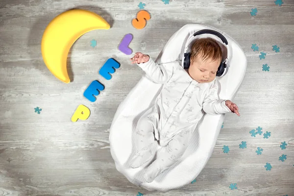 Neugeborenes schläft in einer speziellen orthopädischen Matratze Babykokon, auf einem Holzboden herum bunte Buchstaben. Ruhiger und gesunder Schlaf bei Neugeborenen. — Stockfoto