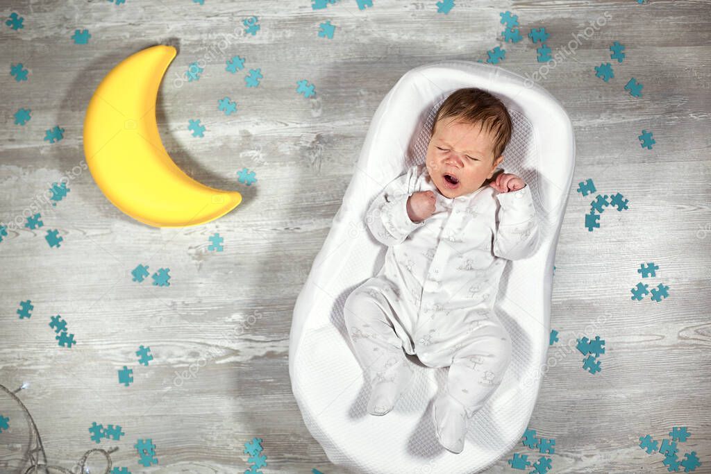 Newborn baby yawns in a special orthopedic mattress Baby cocoon, on a wooden floor, toy moon and puzzles around. Calm and healthy sleep in newborns.
