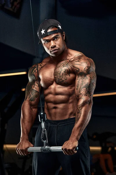 L'homme afro fort et musclé s'entraîne sur des équipements modernes dans la salle de gym. Portrait de musclé pompé entraîneur de conditionnement physique — Photo